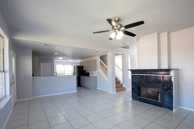 unfurnished living room featuring a fireplace, a textured ceiling, ceiling fan, and light tile patterned floors