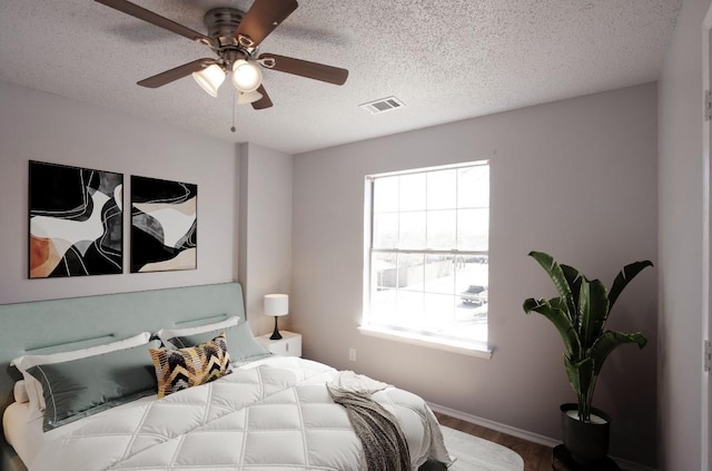 bedroom featuring a textured ceiling, visible vents, wood finished floors, and multiple windows