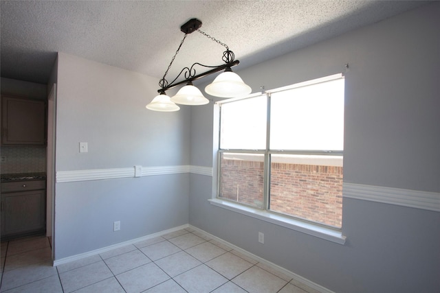 unfurnished dining area featuring light tile patterned flooring, a textured ceiling, a wealth of natural light, and baseboards
