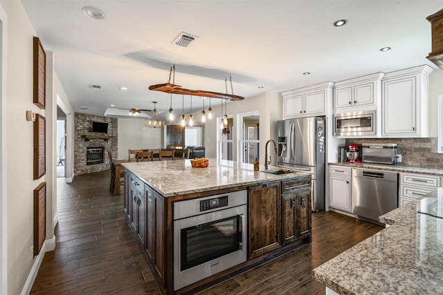 161 Mariah Dr, Weatherford, TX 76087 - kitchen with appliances with stainless steel finishes, open floor plan, a fireplace, an island with sink, and white cabinetry