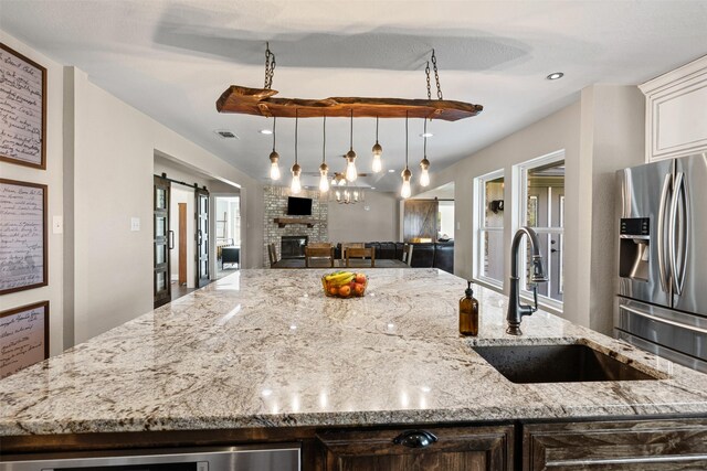 161 Mariah Dr, Weatherford, TX 76087 - kitchen featuring stainless steel fridge, a sink, an island with sink, a fireplace, and light stone countertops
