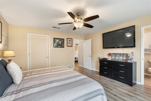 bedroom with a ceiling fan, ensuite bathroom, light wood finished floors, baseboards, and visible vents