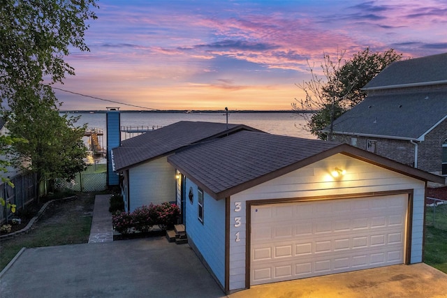 view of front facade featuring roof with shingles, fence, a garage, and a water view