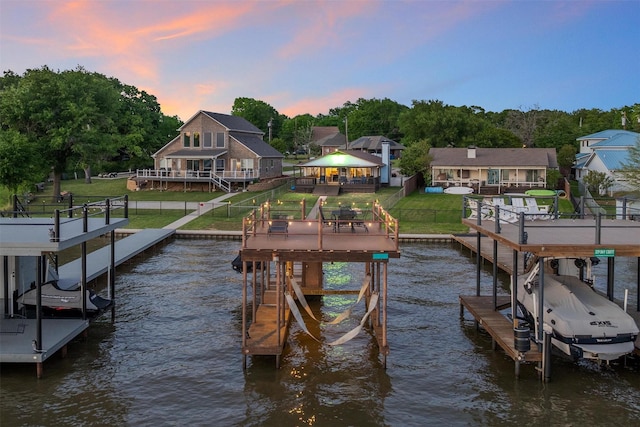 view of dock featuring a deck with water view, fence, boat lift, and a yard