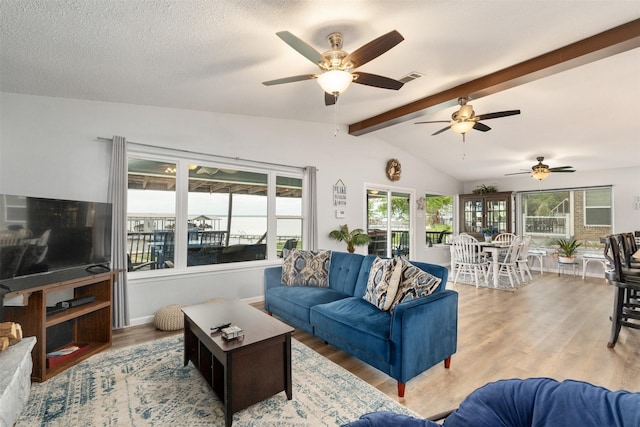 living area featuring wood finished floors, vaulted ceiling with beams, a ceiling fan, and visible vents