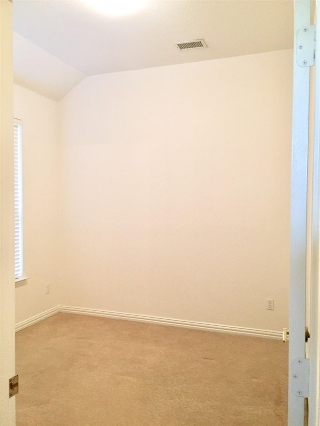 spare room with light carpet, baseboards, vaulted ceiling, and visible vents