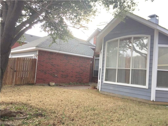 view of property exterior featuring fence, brick siding, a shingled roof, a yard, and a chimney