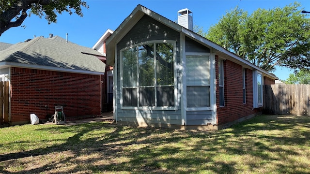rear view of property with a lawn, a chimney, fence, and brick siding