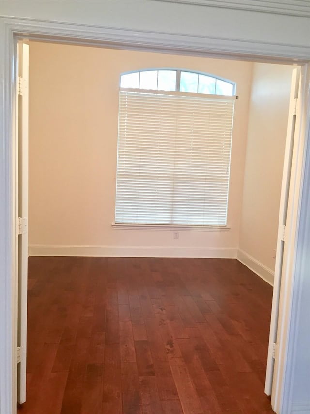 empty room featuring baseboards and dark wood finished floors