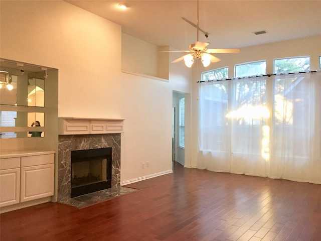 unfurnished living room featuring visible vents, a high end fireplace, baseboards, ceiling fan, and dark wood finished floors