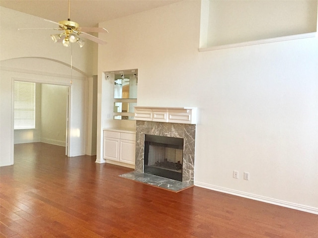 unfurnished living room featuring high vaulted ceiling, a high end fireplace, baseboards, ceiling fan, and wood finished floors