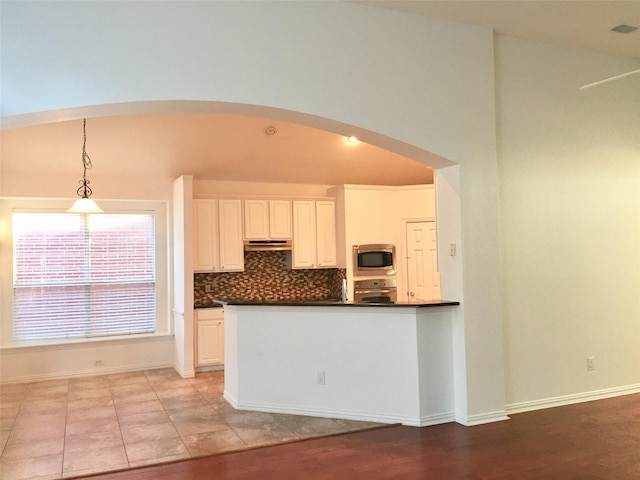 kitchen featuring stainless steel appliances, dark countertops, tasteful backsplash, arched walkways, and decorative light fixtures