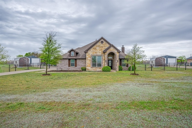 french country home with stone siding, fence, a chimney, a front yard, and brick siding