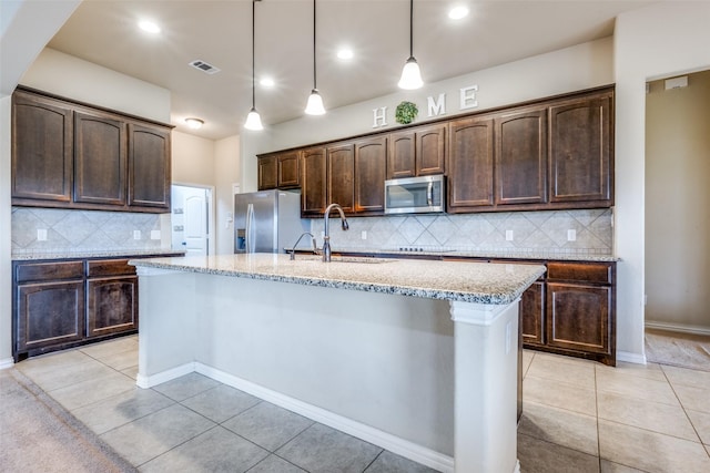 kitchen with an island with sink, stainless steel appliances, dark brown cabinets, and light tile patterned floors