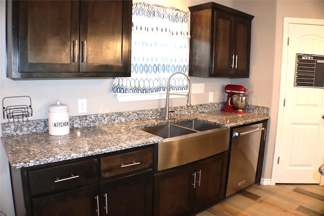 kitchen with dark stone counters, light wood-style floors, a sink, and dishwasher