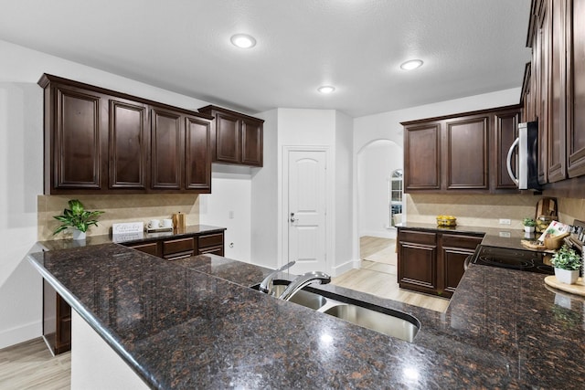 kitchen featuring dark brown cabinetry, backsplash, arched walkways, a sink, and stainless steel microwave
