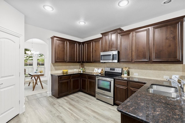 kitchen featuring dark brown cabinets, dark stone counters, arched walkways, a sink, and stainless steel appliances