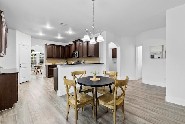 dining space featuring arched walkways, a chandelier, light wood finished floors, and visible vents