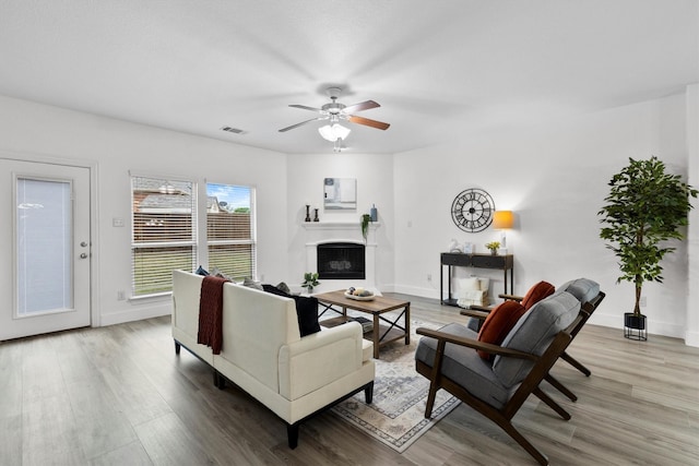 living room with a fireplace, a ceiling fan, baseboards, wood finished floors, and visible vents
