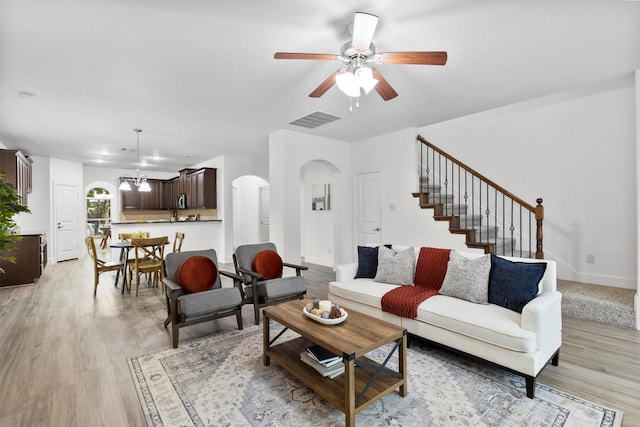 living room featuring visible vents, arched walkways, ceiling fan with notable chandelier, and light wood-type flooring
