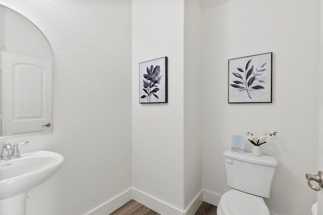 half bath with baseboards, a sink, wood finished floors, and toilet