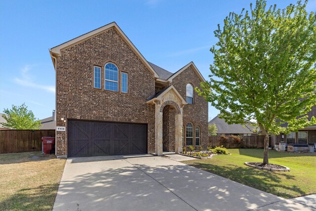 traditional-style home with a garage, fence, a front yard, brick siding, and driveway