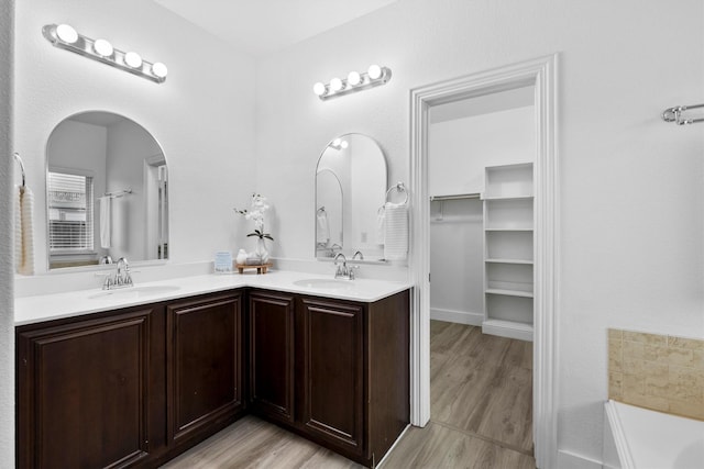 full bath featuring a sink, a bathing tub, double vanity, and wood finished floors