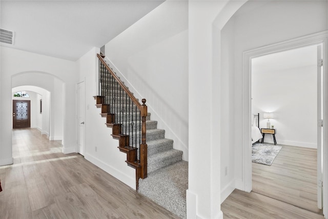 stairway with arched walkways, baseboards, visible vents, and wood finished floors