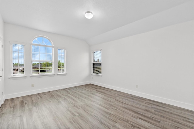 empty room with baseboards, vaulted ceiling, and wood finished floors