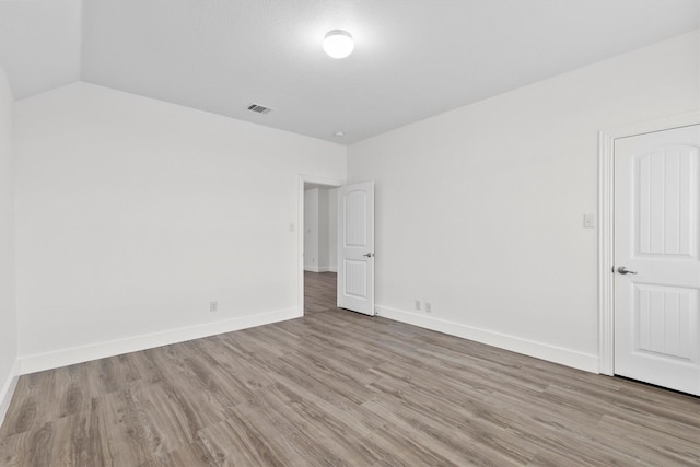 unfurnished room featuring baseboards, vaulted ceiling, wood finished floors, and visible vents