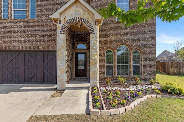 property entrance with brick siding, fence, stone siding, and concrete driveway