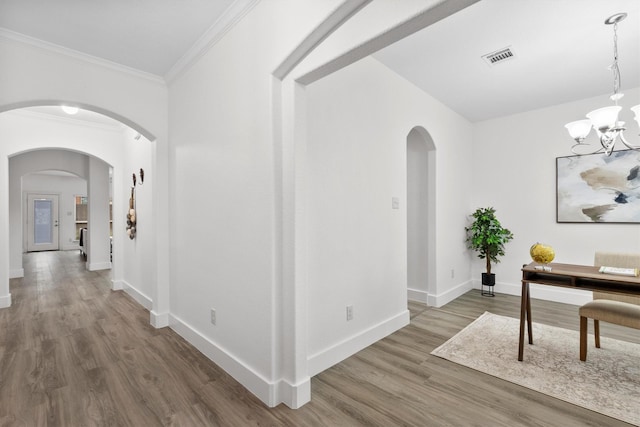 hall with a notable chandelier, arched walkways, baseboards, wood finished floors, and visible vents