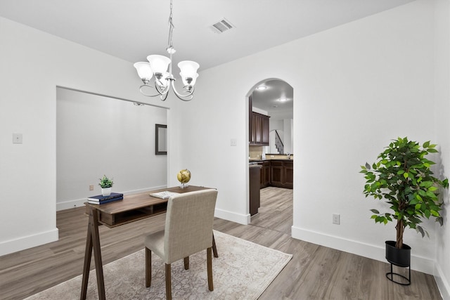 dining space featuring visible vents, baseboards, a chandelier, arched walkways, and light wood-style flooring
