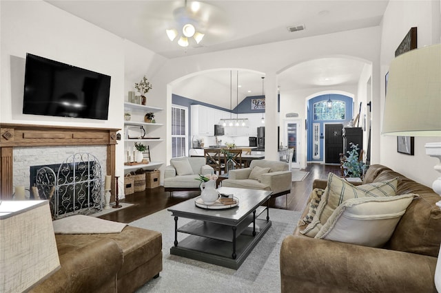 living room with wood finished floors, visible vents, a ceiling fan, arched walkways, and a fireplace