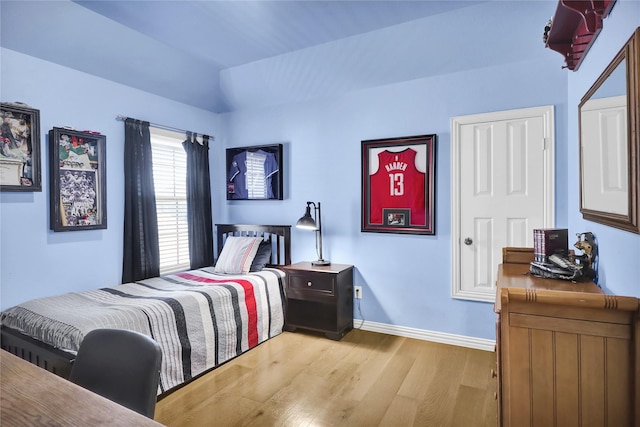 bedroom with baseboards, lofted ceiling, and light wood-style flooring