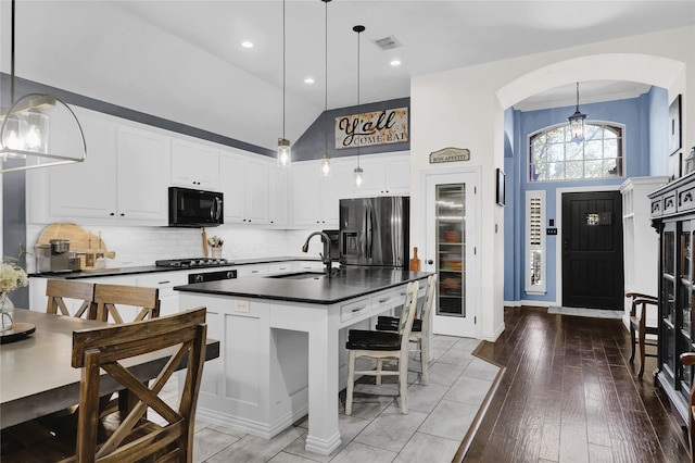 kitchen with dark countertops, a sink, black microwave, stainless steel fridge with ice dispenser, and visible vents