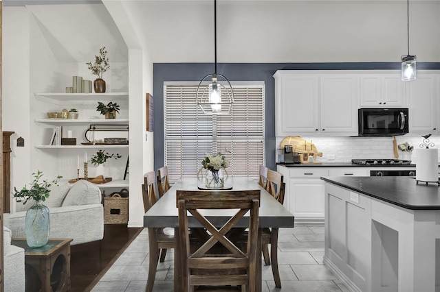 kitchen with dark countertops, black microwave, decorative backsplash, hanging light fixtures, and white cabinetry