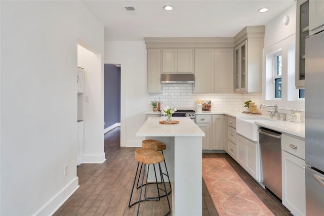 930 N Clinton Ave, Dallas, TX 75208 - kitchen featuring appliances with stainless steel finishes, under cabinet range hood, a sink, a breakfast bar area, and decorative backsplash