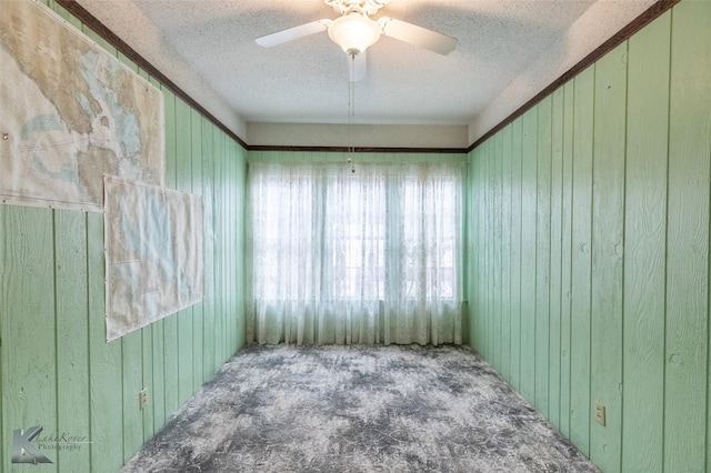 carpeted spare room with a textured ceiling, a ceiling fan, and wooden walls