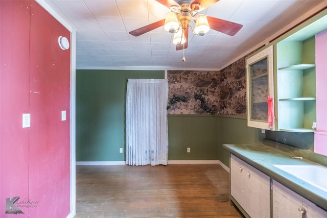 kitchen featuring a wainscoted wall, ceiling fan, wood finished floors, wallpapered walls, and a sink