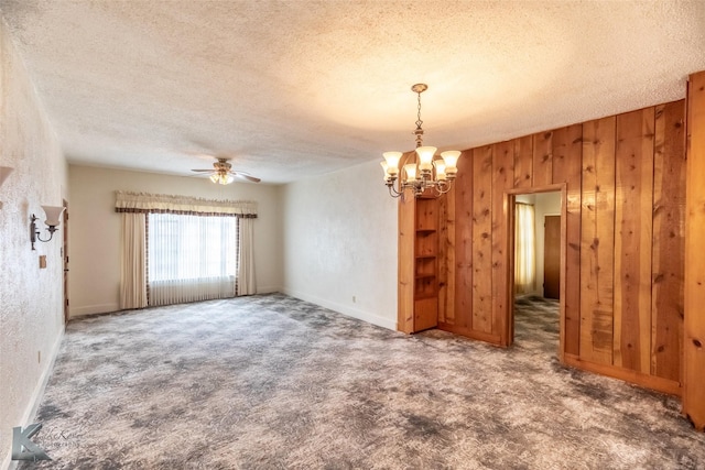 unfurnished room featuring carpet floors, ceiling fan with notable chandelier, wooden walls, and a textured ceiling