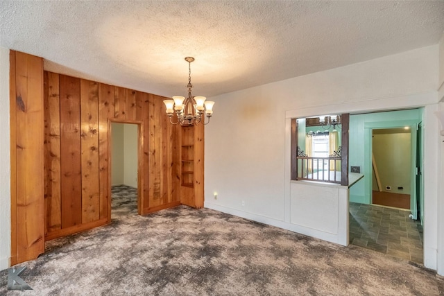 carpeted spare room featuring a textured ceiling, wooden walls, and a chandelier