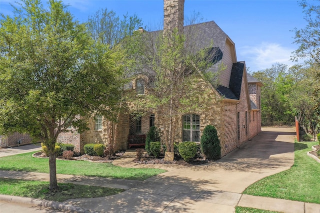 view of front of house with a shingled roof, a front yard, brick siding, and concrete driveway