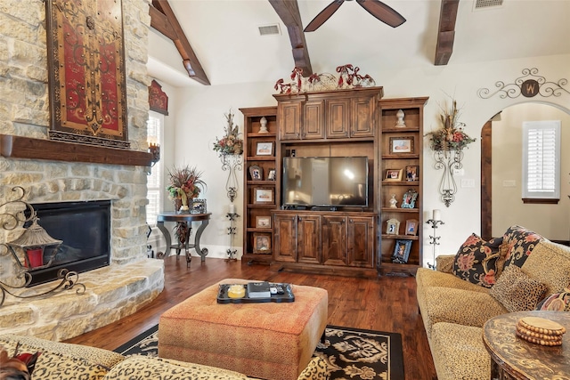 living room with lofted ceiling with beams, a stone fireplace, visible vents, ceiling fan, and dark wood-style flooring