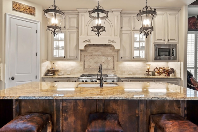 kitchen featuring a kitchen bar, tasteful backsplash, stainless steel microwave, under cabinet range hood, and light stone countertops