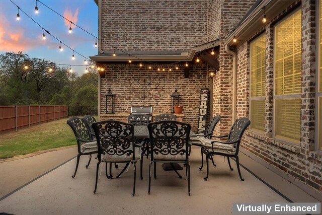 patio terrace at dusk with grilling area, outdoor dining area, and fence