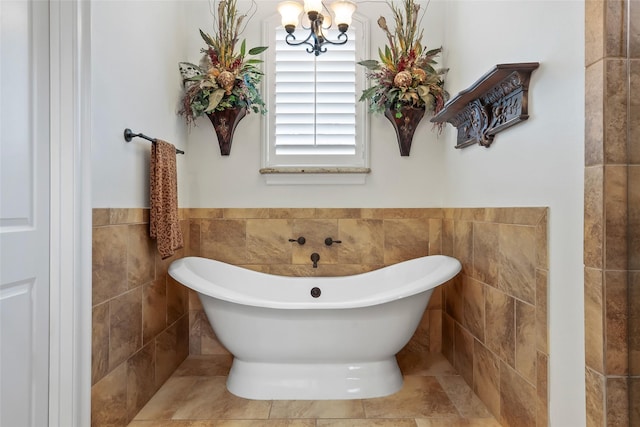 full bathroom featuring tile walls, a wainscoted wall, a chandelier, and a soaking tub