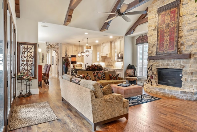 living room featuring a fireplace, wood finished floors, beamed ceiling, arched walkways, and ceiling fan