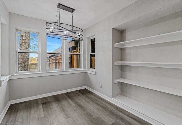 unfurnished dining area featuring an inviting chandelier, baseboards, and dark wood finished floors