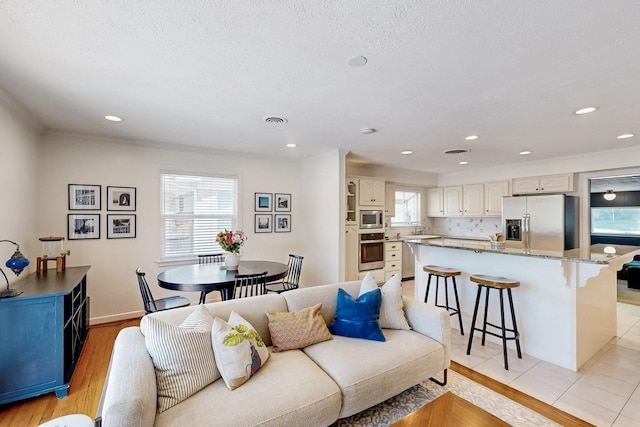 living area featuring recessed lighting, visible vents, ornamental molding, baseboards, and light wood-style flooring